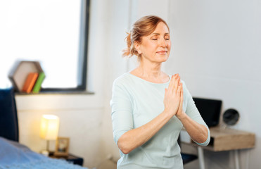 Appealing mature lady being in peaceful state while meditating