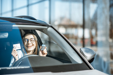 Portrait of a young woman with excited emotions holding keys and license in the new car