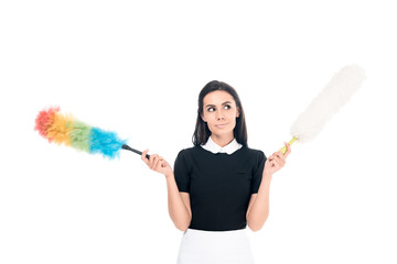 Dreamy brunette maid in uniform holding dusters isolated on white