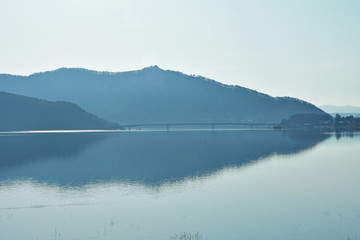 The mountain background with a bridge across the large lake has a steady water.