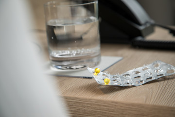 Pillen Blister mit gelben Tabletten und Wasser Glas auf Holz Nachttisch