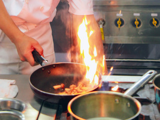 Chef cooking with flame in a frying pan on a kitchen stove