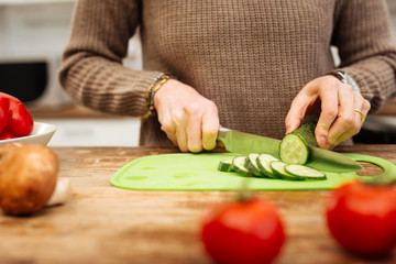 Accurate woman staying in kitchen and chopping ingredients for salad