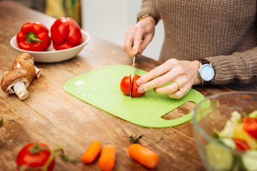 Attentive mature woman with watch on her wrist cutting vegetables