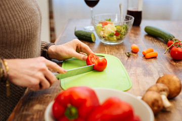 Pleasant woman carrying long metal knife and chopping tomato