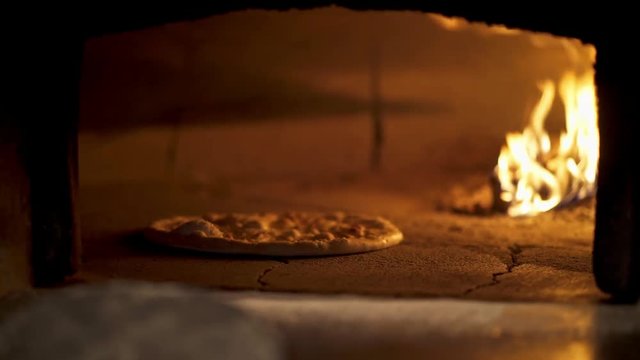 Italian pizza focaccia cooking in the oven with burning fire. Italian cook twisting pizza inside of the oven with fire. Ready hand made pizza focaccia in the oven