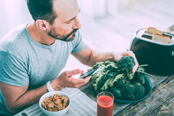 Modern handsome man making a photo of broccoli
