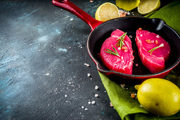 Fresh raw tuna fish steaks with ingredients for cooking, on frying pan, dark blue concrete...