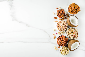 Various types of nuts - walnuts, pecans, peanuts, hazelnuts, coconut, almonds, cashews, in bowls, on a white marble table top view