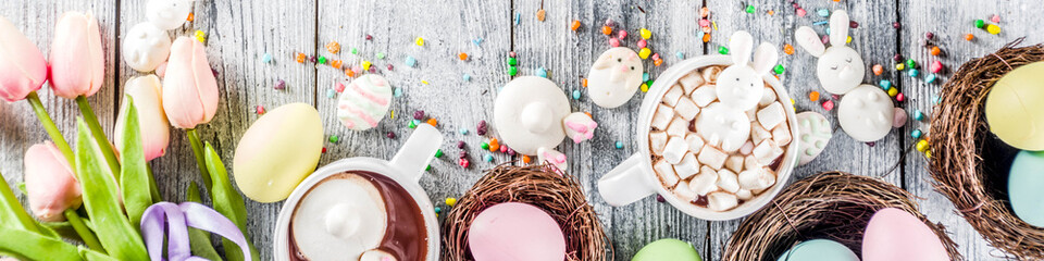 Easter funny kids food and drink concept, sweet hot chocolate with marshmallow bunny rabbits and easter eggs, wooden background copy space top view banner