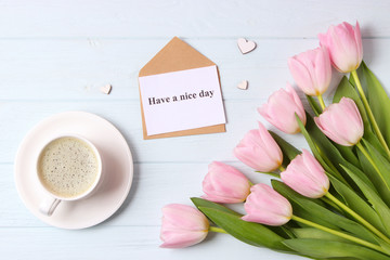  Cup of coffee, a bouquet of flowers and a card with the inscription "have a nice day" on a wooden background, top view.