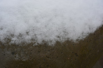 Beautiful snow background, melting snow on a concrete structure, concrete wall with gray-brown color.