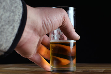Male hand taking a glass of beer from wood table. Black background with copy space.