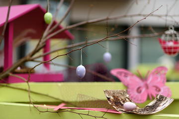 Easter decorations on the street of small town in France. Easter painted eggs hanging on a branch of tree and wooden butterfly toys as decoration.