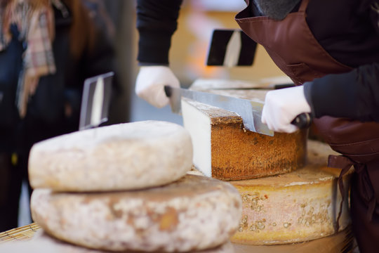 Seller cutting organic cheese on farmer market in Strasbourg, France. Typical European local farmer market