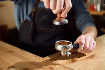 Fototapeta na wymiar Barista presses ground coffee using tamper in a coffe shop