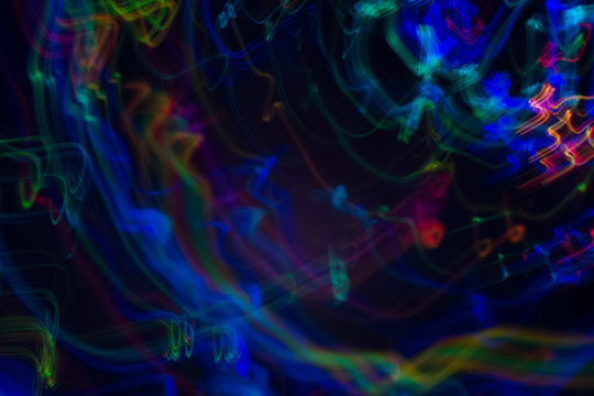 Blurred neon lights in motion. Thin curved multicolor lines on dark background. Lens flare effect.