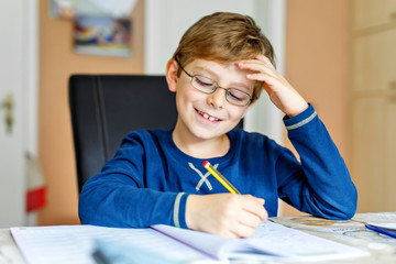 Naklejka na ściany i meble Portrait of cute school kid boy wearing glasses at home making homework. Little concentrated child writing with colorful pencils, indoors. Elementary school and education