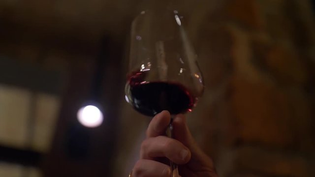 A man's hand holds a glass of red wine and twists it. Glass goblet. Wine tasting. Shake a drink in a glass, panoramic shot.