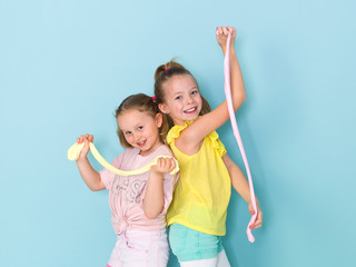two beautiful girls playing with homemade slime and having a lot of fun in front of blue background