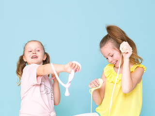 two beautiful girls playing with homemade slime and having a lot of fun in front of blue background