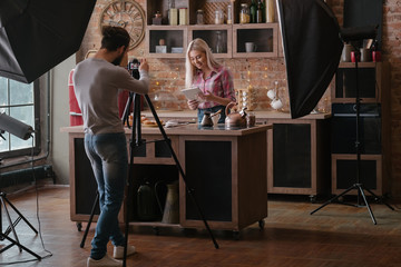 Man shooting food blogger. Photo session. Woman at kitchen counter with tablet. Backstage...