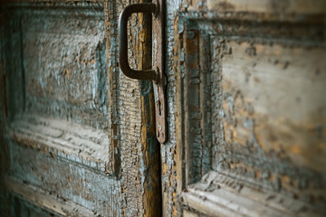 An old medieval closed door with a crumbling layer of blue paint, with a rusty iron handle and a keyhole, which you want to peek.