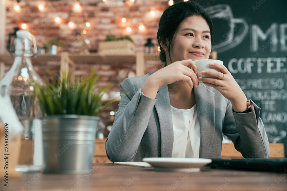 Wall mural Young start up entrepreneur asian woman sits in cafe with laptop computer looks on side thoughtful. businesswoman smiling drinking coffee happy thinking daydreaming working on business idea.