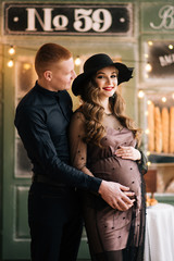 Beautiful young, stylish pregnant girl with her husband on the background of a French bakery