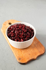 Dried cranberries in a bowl on rustic wooden board over gray surface, side view. Close-up.