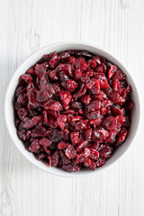 Dried cranberries in a bowl over white wooden surface, top view. From above, overhead, flat lay. Closeup.