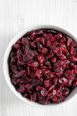 Dried cranberries in a bowl over white wooden surface, top view. From above, overhead, flat lay. Close-up.