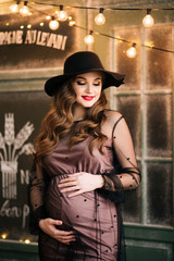 Beautiful young, stylish pregnant girl, in a black dress and hat, in the interior of a French bakery