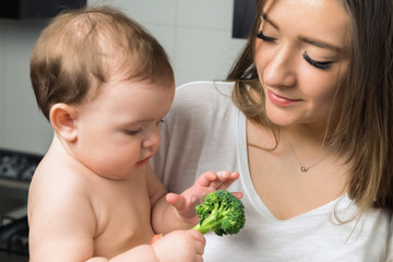 Young mother feeds baby broccoli.