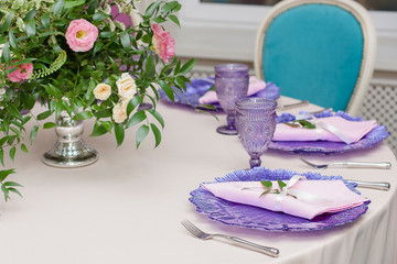 Bouquet of flowers on the table on the wedding day. Lilac plates and glasses on the festive table