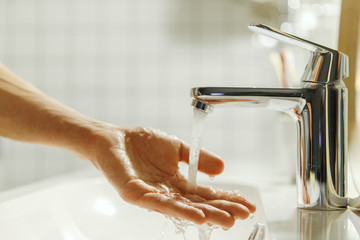 Man washing and cleaning her hand in bathroom, soft focus. Closeup of fingers under flowing tap...