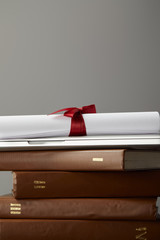 Brown books, laptop and diploma with red ribbon isolated on grey