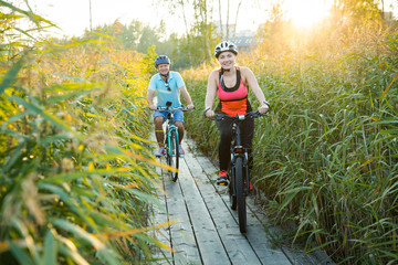 Happy couple working out together, leisure activity. Man and woman in helmets traveling by bikes on...