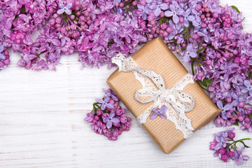 Lilac flowers and cute gift box on white wooden background, copy space. Mother's day background