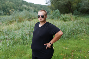 Naklejka na ściany i meble fat guy in black clothes in the summer park