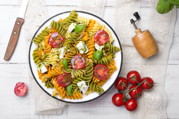 Italian food - Salad with colorful pasta, cherry tomatoes, feta cheese and fresh basil on white wooden background