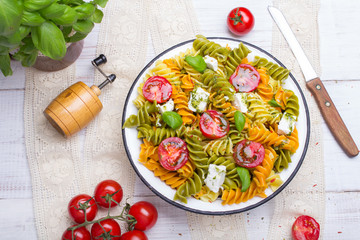 Italian food - Salad with colorful pasta, cherry tomatoes, feta cheese and fresh basil on white wooden background