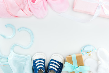 top view of booties and sneakers, pacifier, gift boxes and bonnets on white background