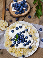 Tasty pasta with fresh organic blueberries and vanilla cream. Sweet dinner on retro wooden table.