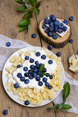 Tasty pasta with fresh organic blueberries and vanilla cream. Sweet dinner on retro wooden table.