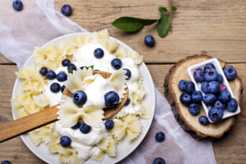 Tasty pasta with fresh organic blueberries and vanilla cream. Sweet dinner on retro wooden table.