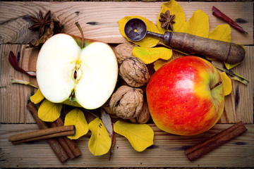 Fototapeta na wymiar Tasty apples, walunts, cinamon and autumn leaves on wooden background