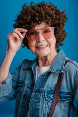 Portrait of old lady wearing fashionable eyeglasses against blue wall