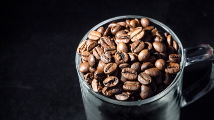 Glass cup of coffee with coffee beans on a dark background, close-up, in a low key