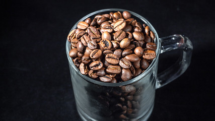 Glass cup of coffee with coffee beans on a dark background, close-up, in a low key